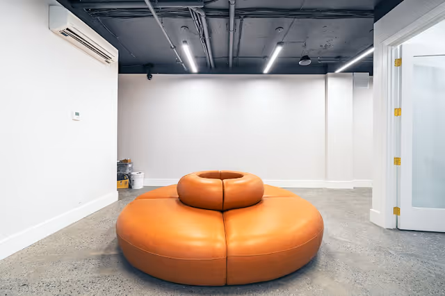 Modern lounge with a large orange circular sofa in a white minimalist room.