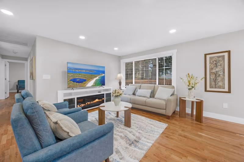 Bright living room with blue couches, TV, fireplace, and large window.