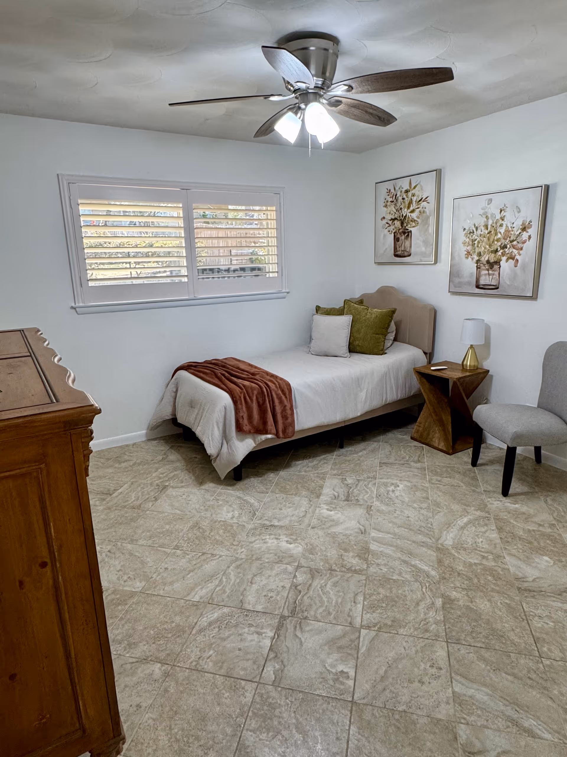 A tidy bedroom in a senior living facility featuring a single bed, nightstand, and window blinds.