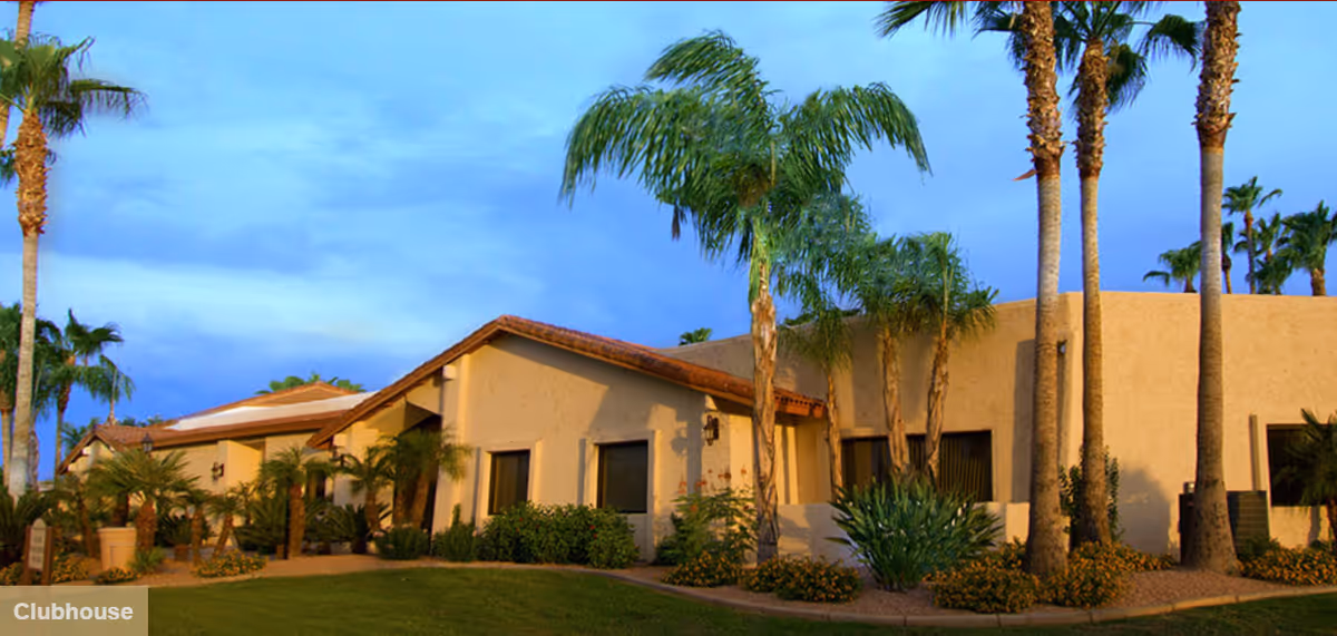 Sunlit exterior of a tan, single-story assisted living building with palm trees.