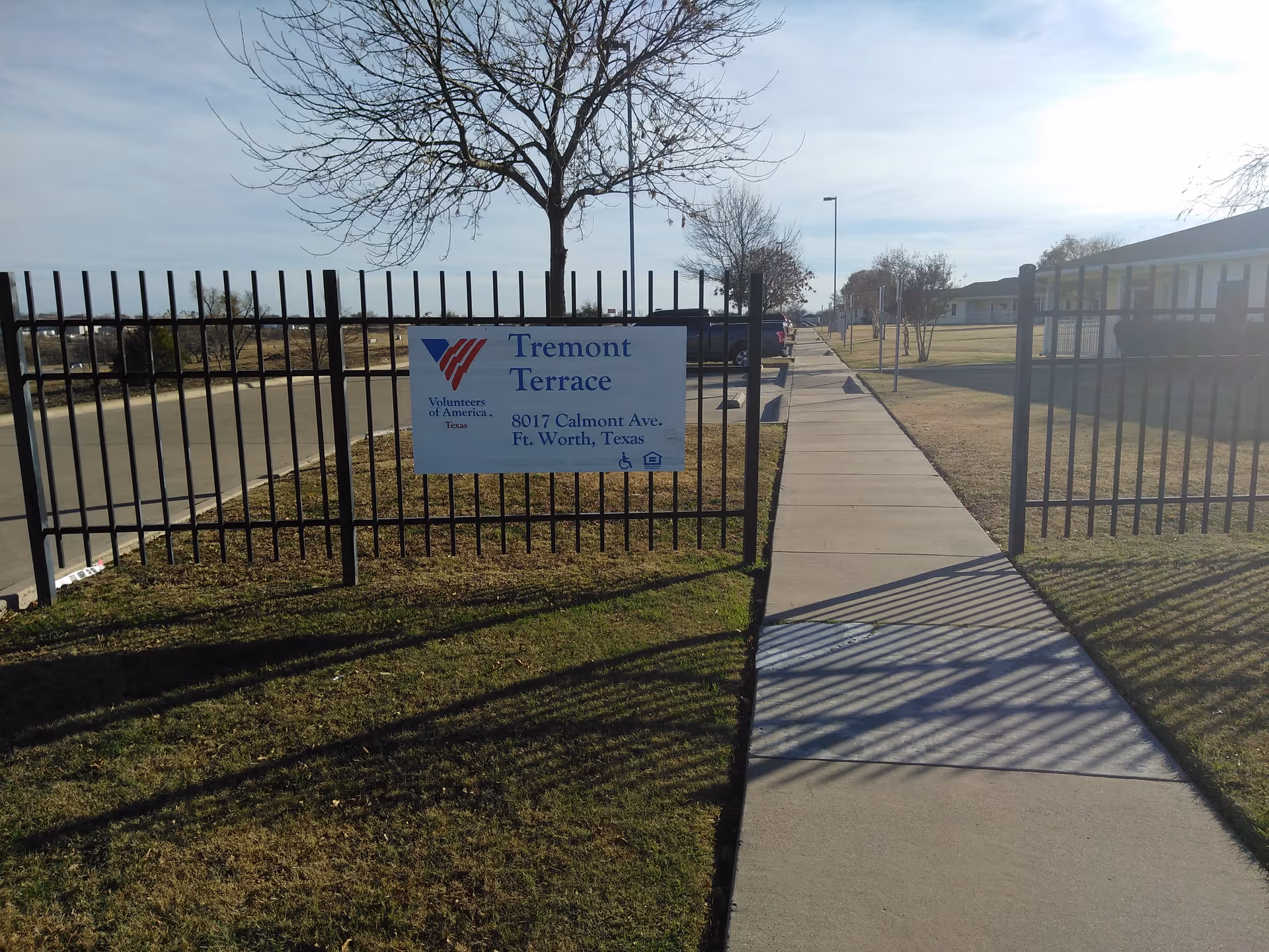 Fence-lined entrance with a Tremont Terrace sign and a sunlit sidewalk along the facility.