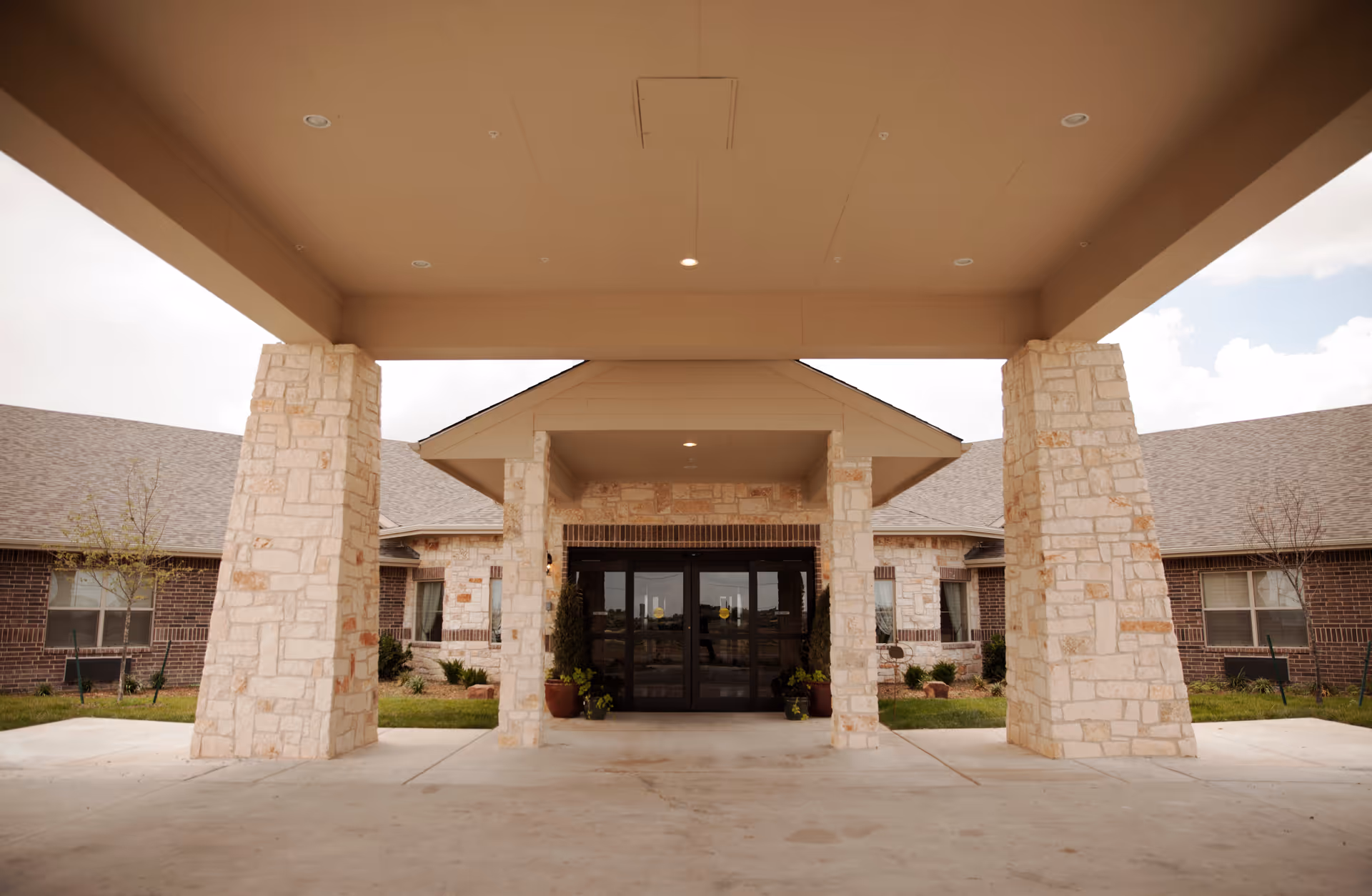 Exterior view of a senior care facility entrance with stone columns and porte-cochere.