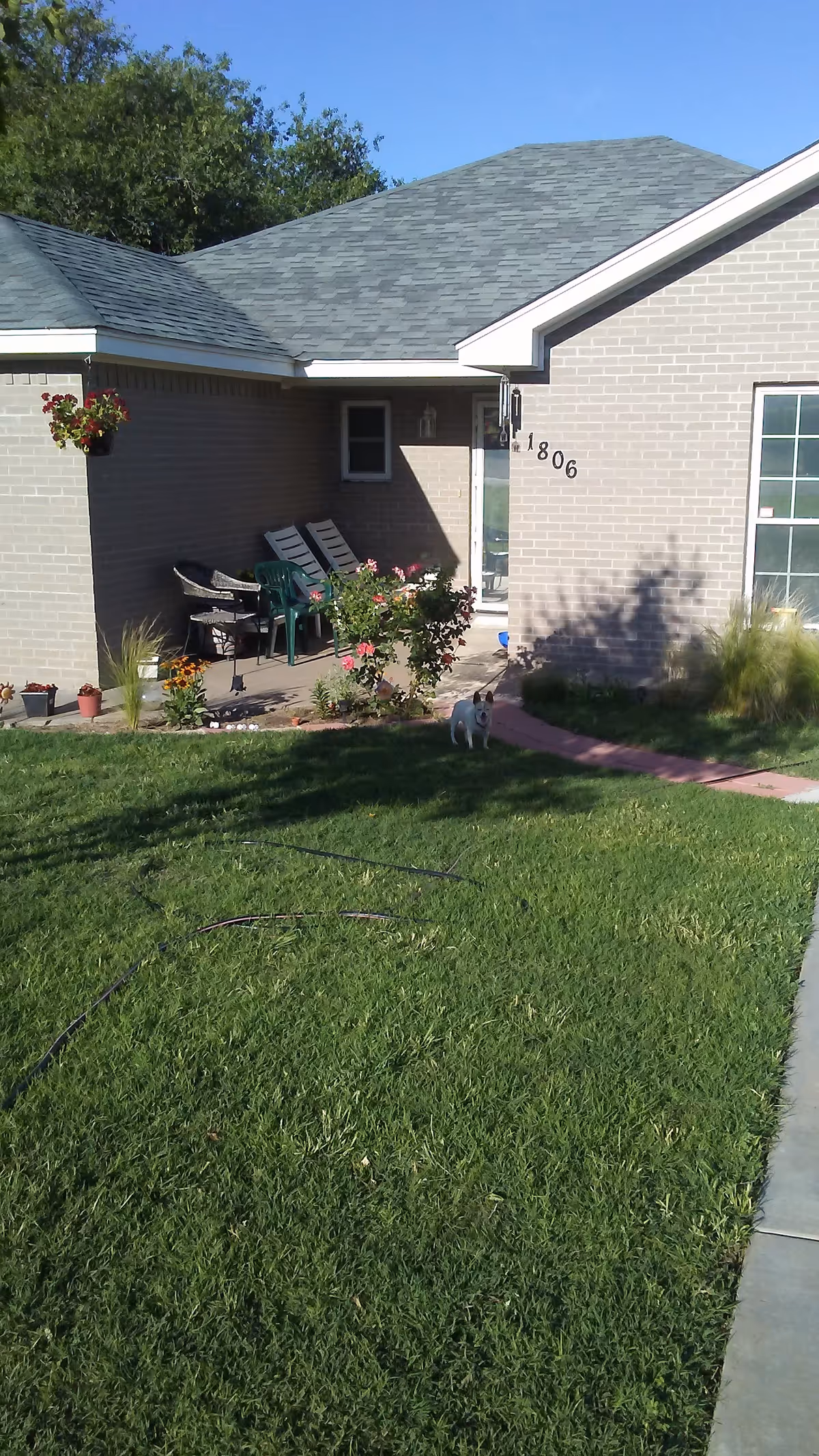 Brick single-story home exterior with a small porch, lawn, and garden seating.