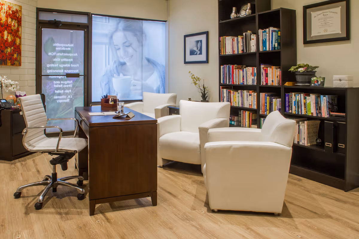 Reception-style sitting area with a desk, white armchairs, an office chair and bookshelves.