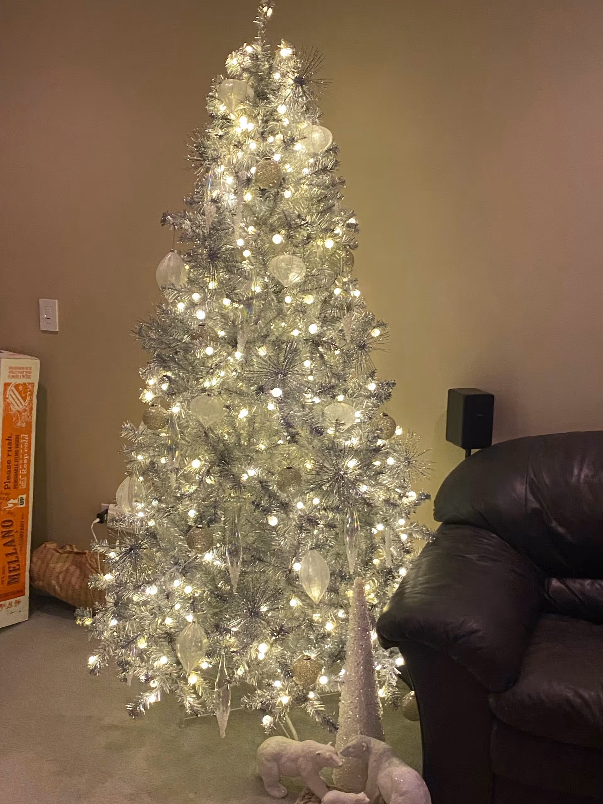 Silver Christmas tree with lights in a living room beside a dark leather chair.