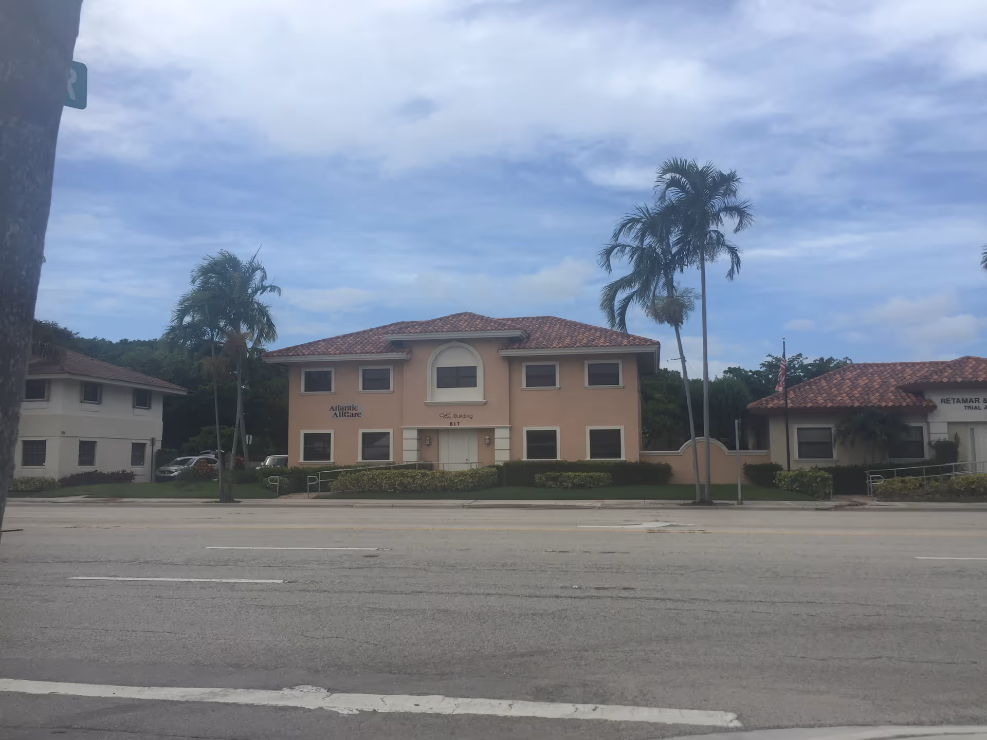 Peach-colored two-story building labeled Atlantic Allcare Inc along a street with palm trees
