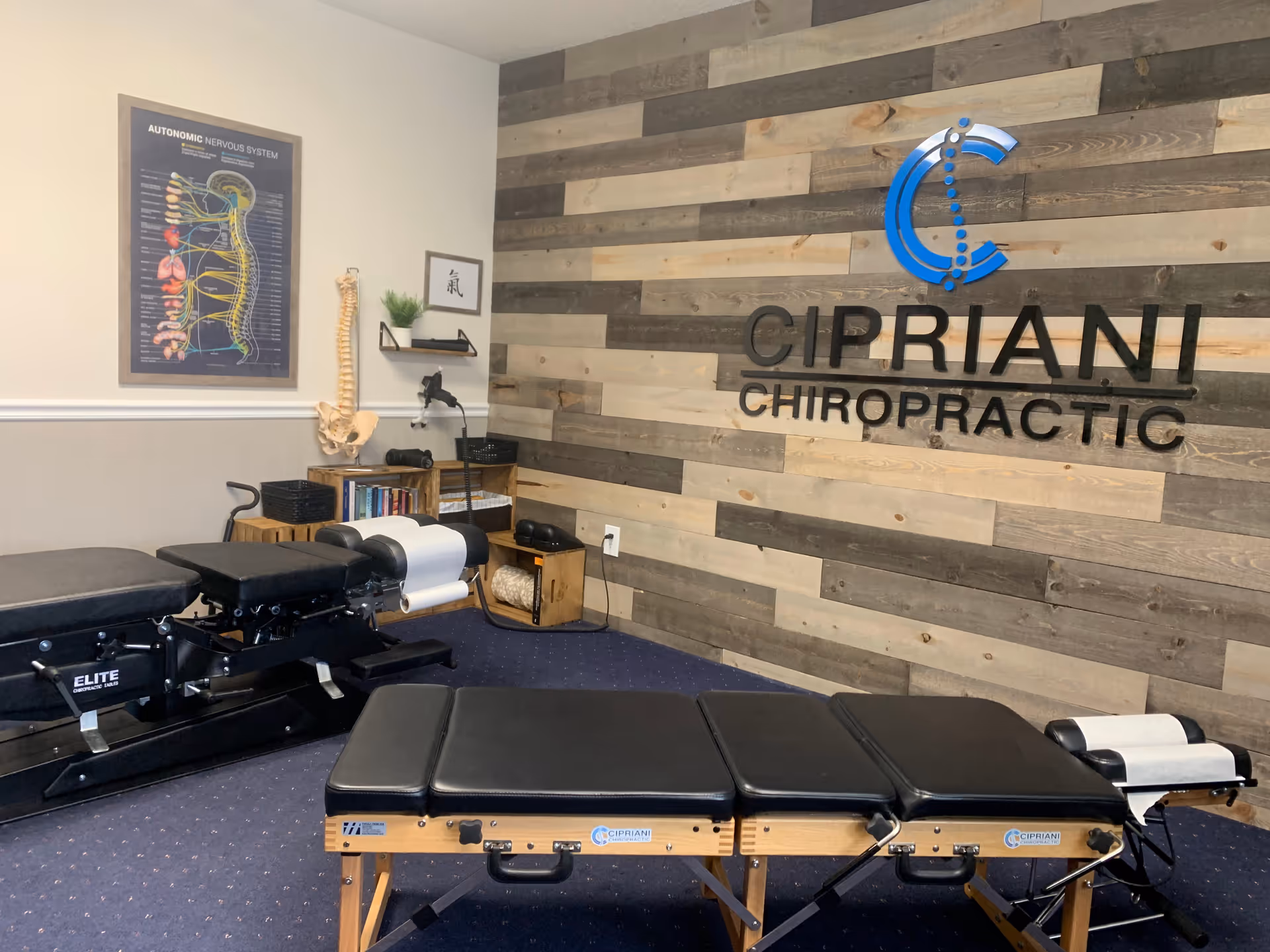 Chiropractic treatment room with tables, equipment, and a Cipriani Chiropractic sign on wood wall.