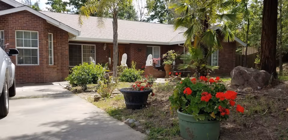 Front exterior of a single-story brick residence with a driveway, potted red flowers, and landscaping.
