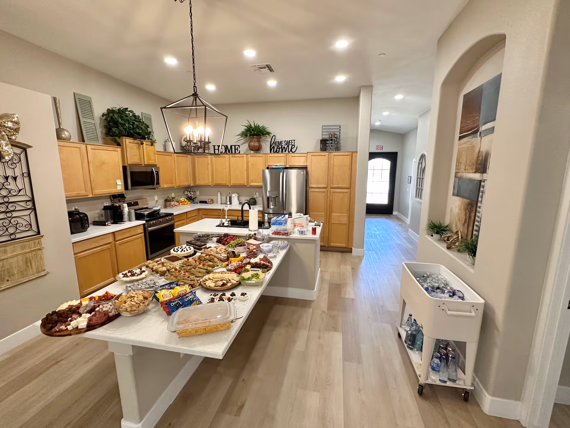 Well-lit communal kitchen with a long island and assorted snacks arranged for an event.