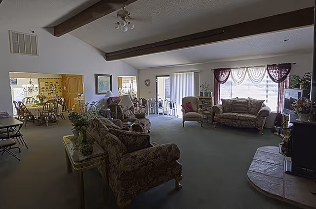 Open living room with floral sofas, armchairs, coffee tables, and large windowed back wall.