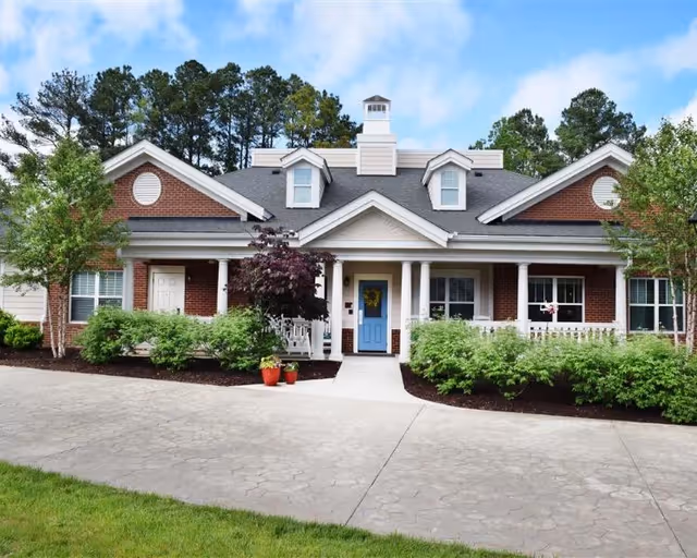 Brick senior living facility exterior with a blue front door, columns, and landscaped entrance.