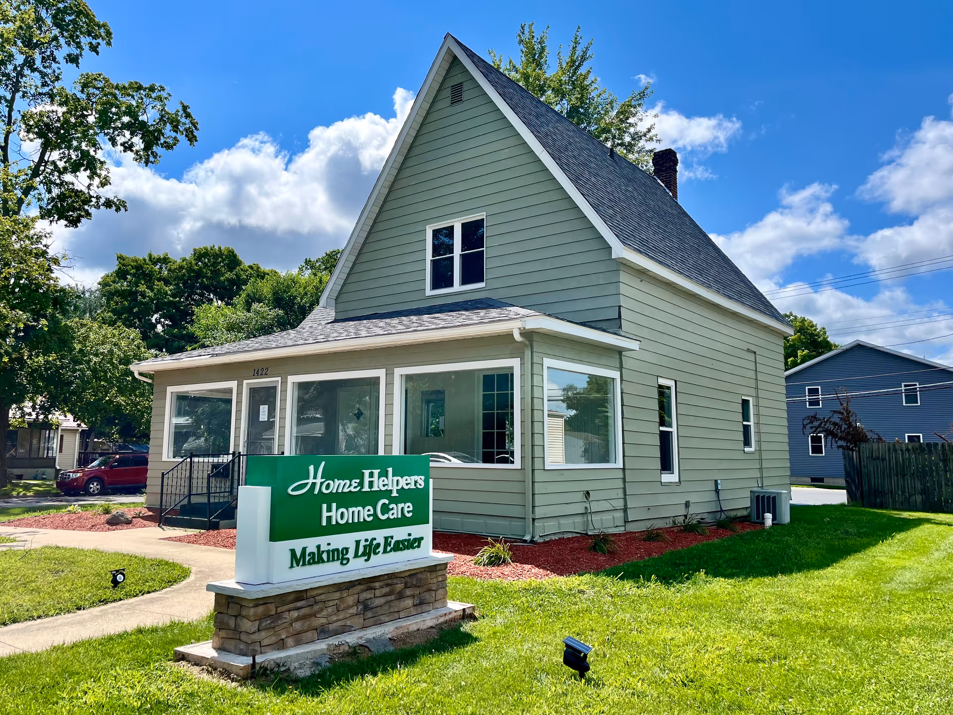 Green Home Helpers Home Care building with sign, blue sky, and manicured lawn.