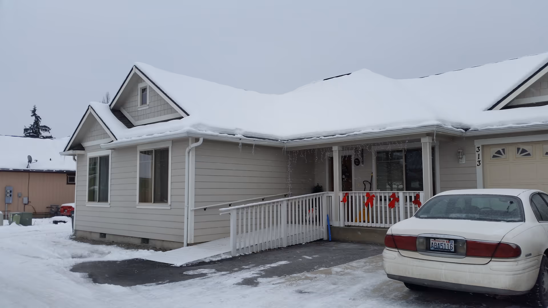 Snow-covered, single-story facility with a front porch, railing, and a parked car in the driveway.