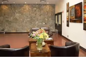 Lobby seating area with leather chairs, wooden coffee table, flowers, and a stone wall.