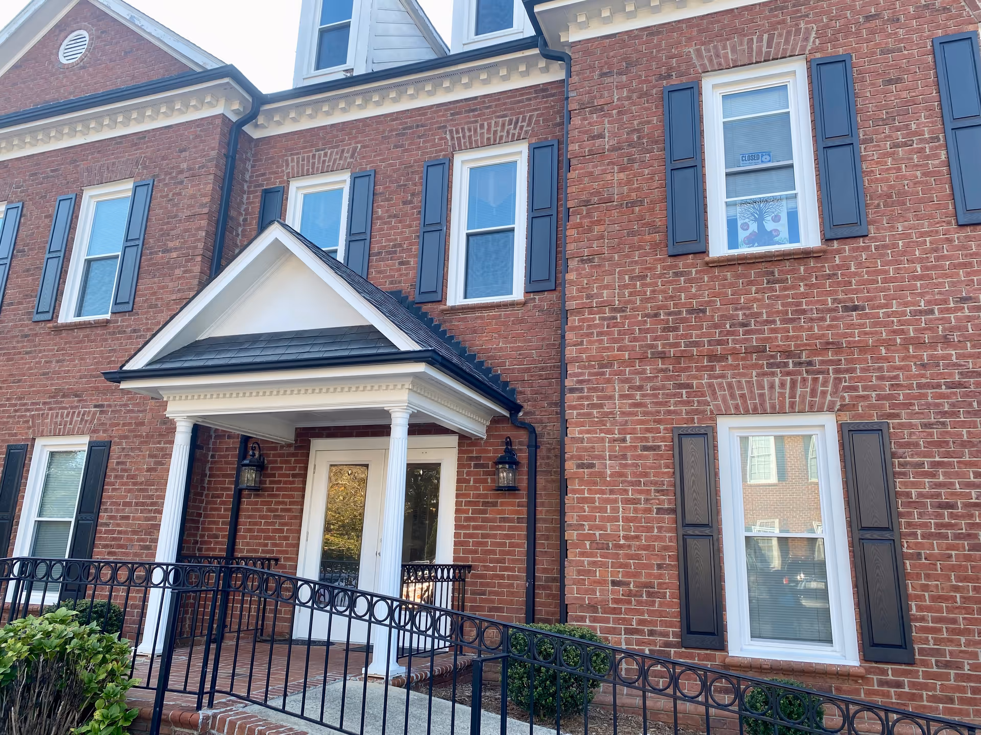 Entrance of brick senior living facility with porch, columns, and black shutters.