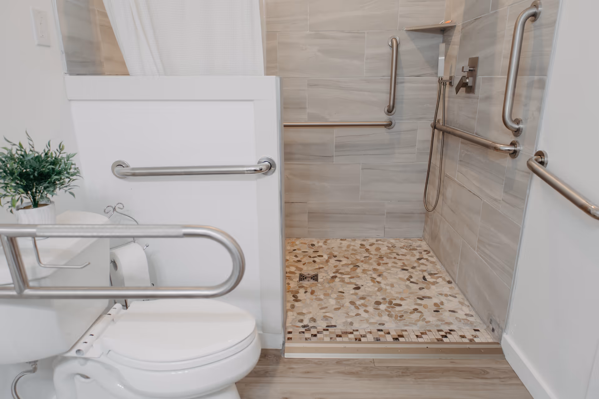 Accessible bathroom with grab bars around toilet and tiled shower.