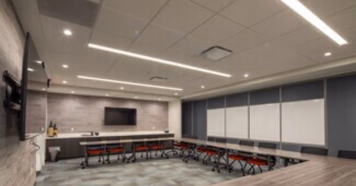Modern conference room with long tables in a U-shaped layout, red chairs, and wall-mounted TV.
