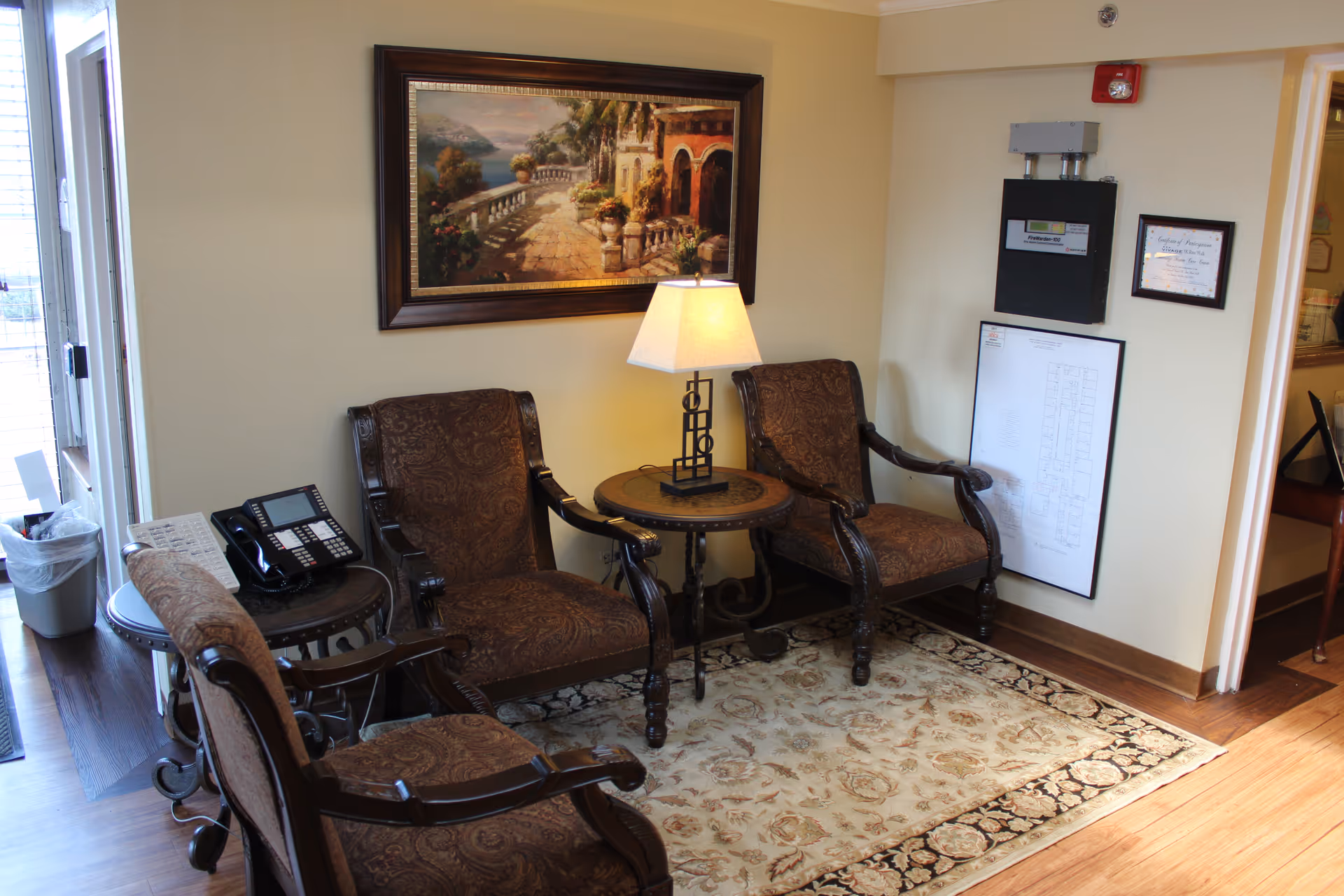 Lounge seating area with four ornate chairs, a round table lamp, and wall art.
