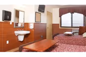Shared resident bedroom with two beds, red bedspreads, and a wall-mounted sink.