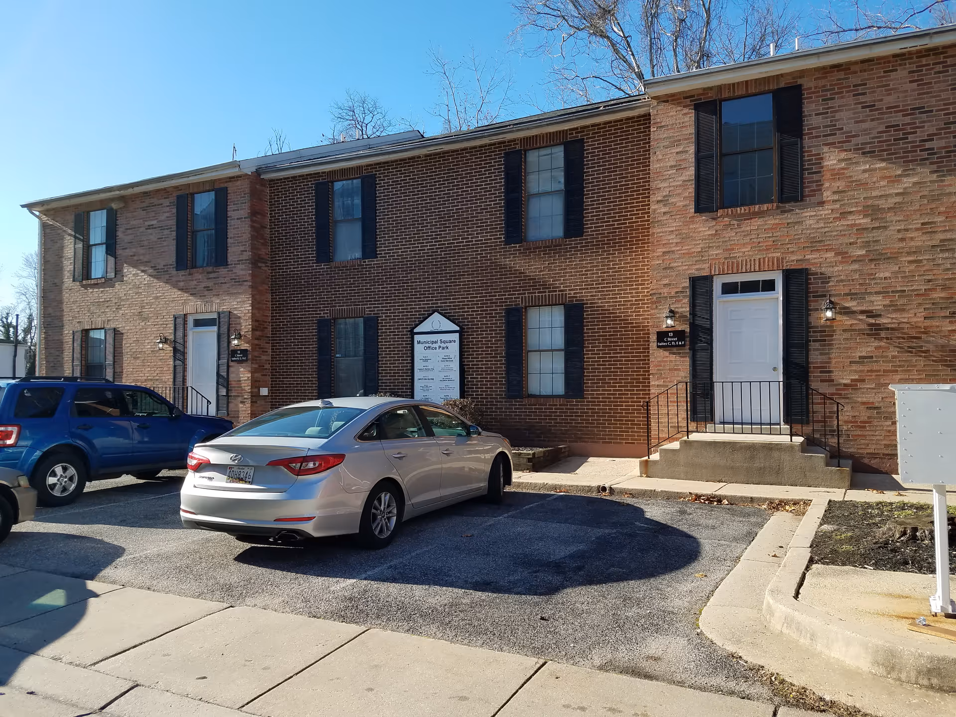 Brick senior living building with parked cars and two front entrances under a clear blue sky