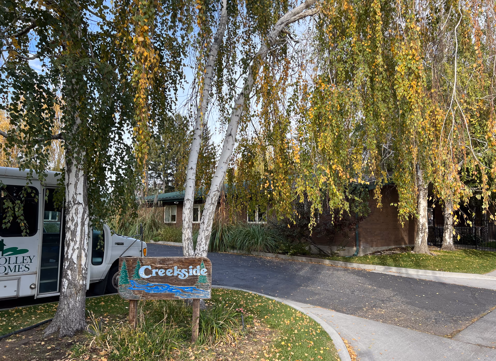 Exterior view of Creekside Residential Care Center with sign, bus, trees, and driveway.