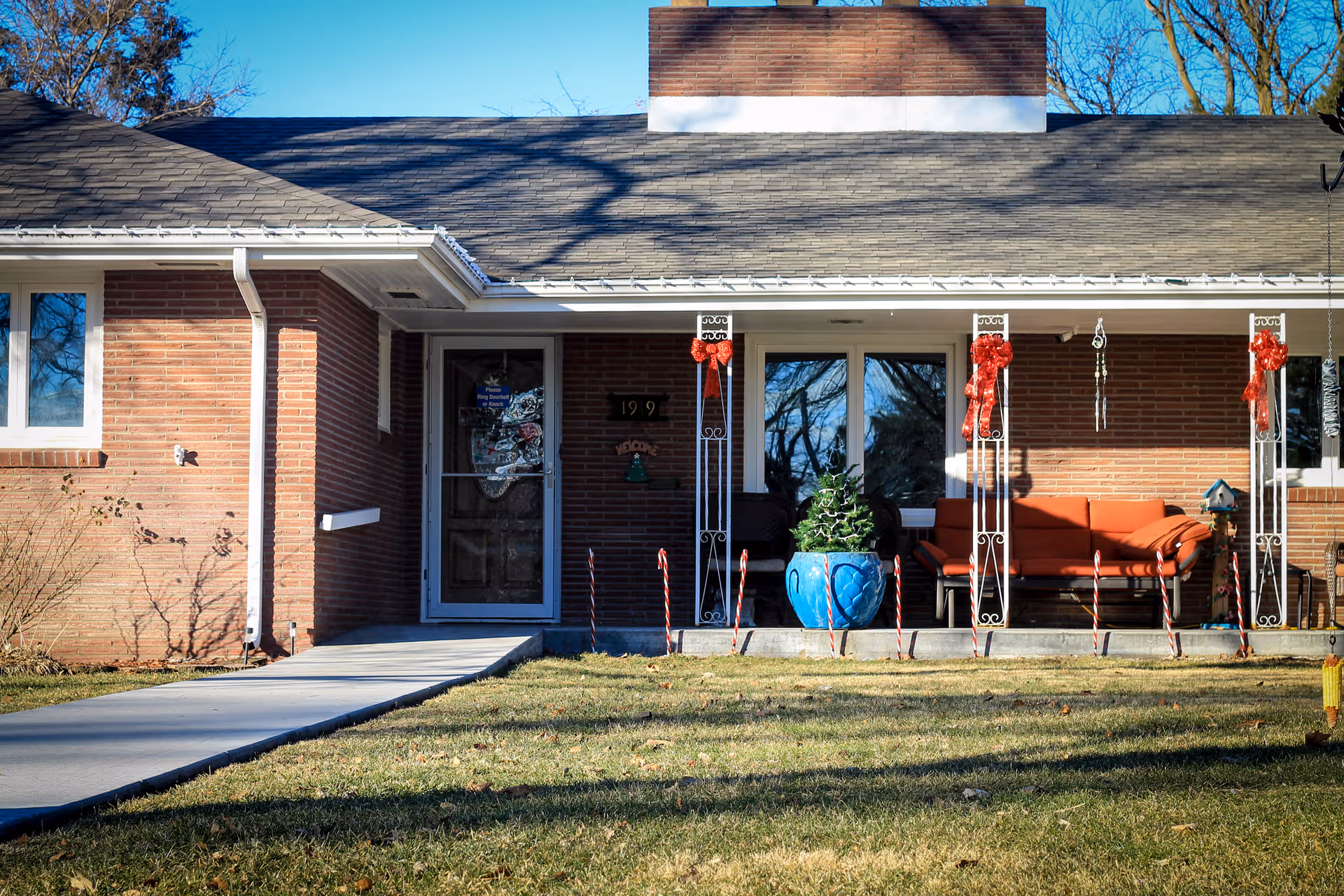 Brick senior living facility front porch with seating, holiday ribbons, and a blue potted plant.