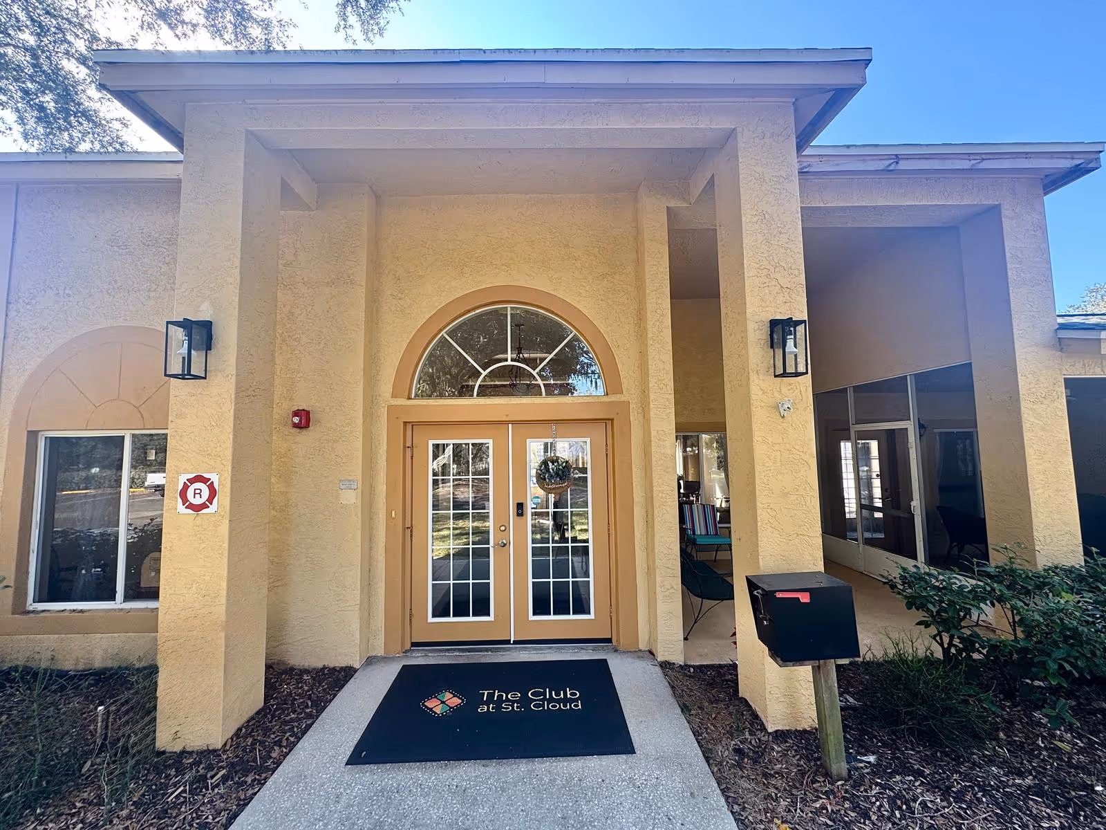 Front entrance of The Club at St. Cloud with double glass doors, stucco columns, and a welcome mat showing the facility name.