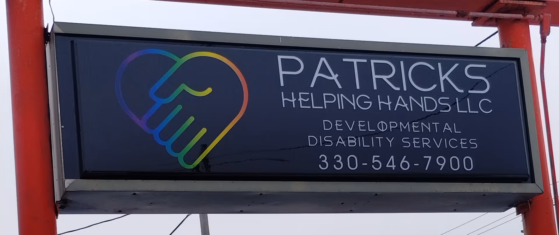 Outdoor signboard for Patrick's Helping Hands LLC featuring a rainbow hand logo and contact number.