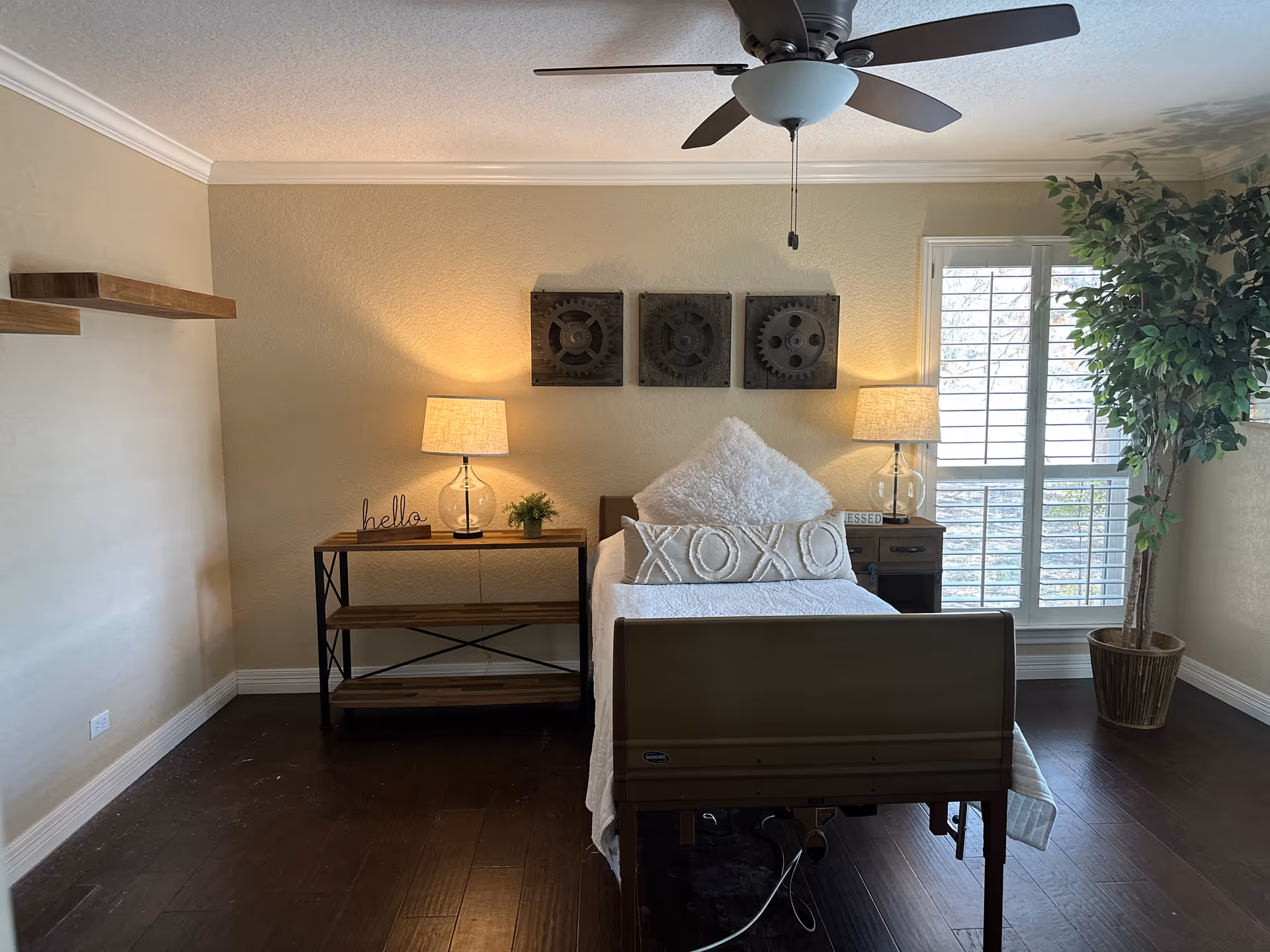 A cozy bedroom with a bed, two nightstands, lamps, a ceiling fan, and a window.