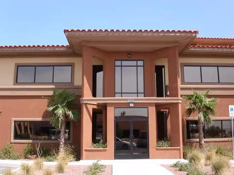 Front view of a brown two-story facility with glass entry and palm trees