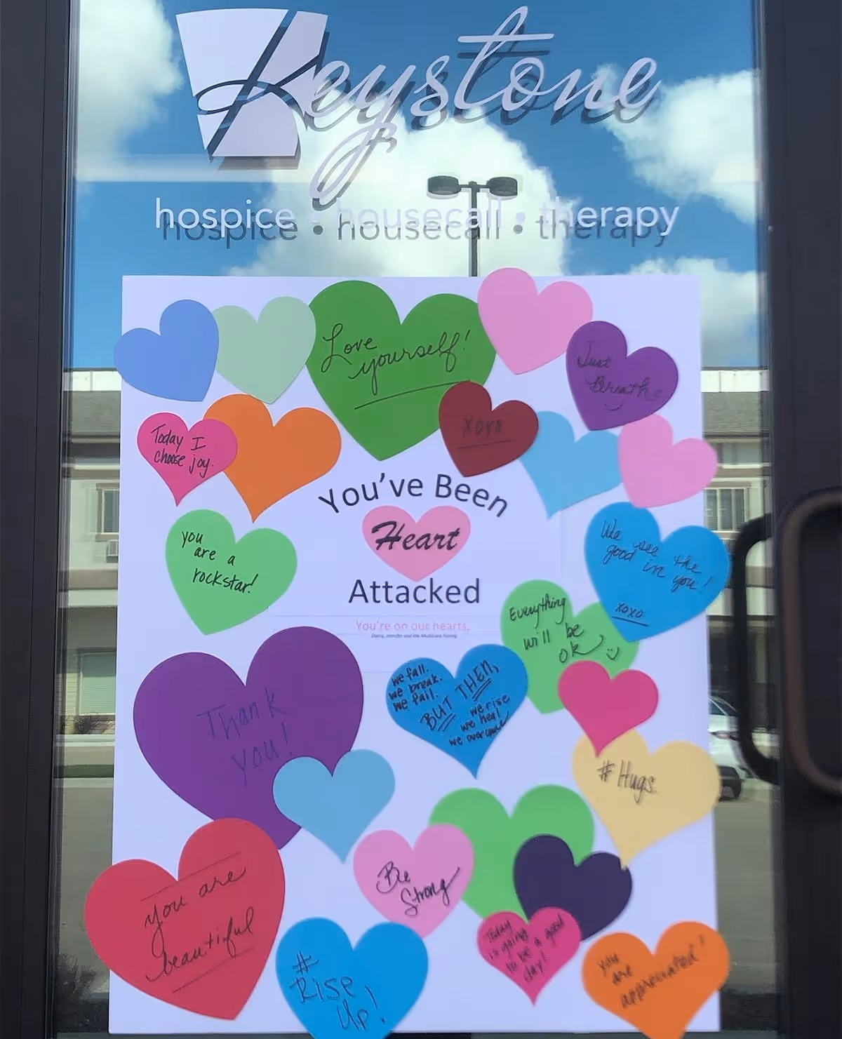 Glass door with Keystone Hospice sign and a colorful heart collage poster.