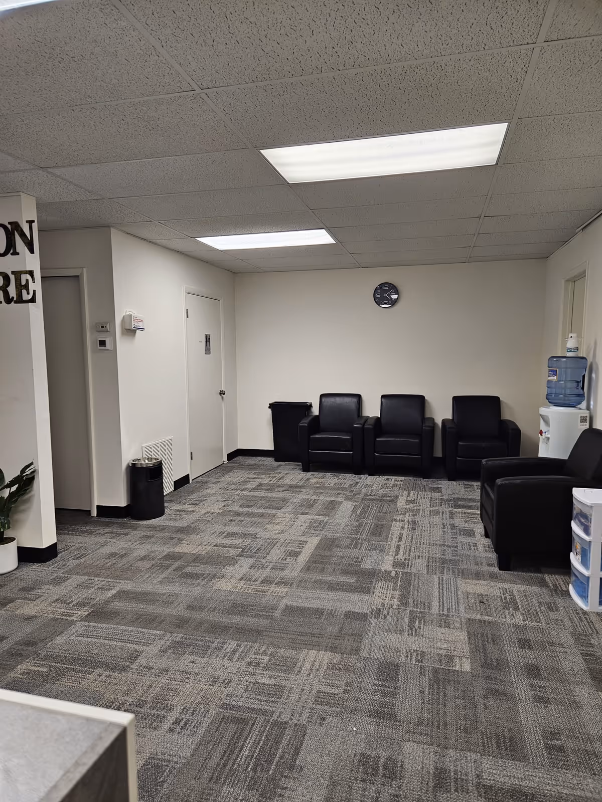 Empty waiting area with black leather chairs, water cooler, and carpet.