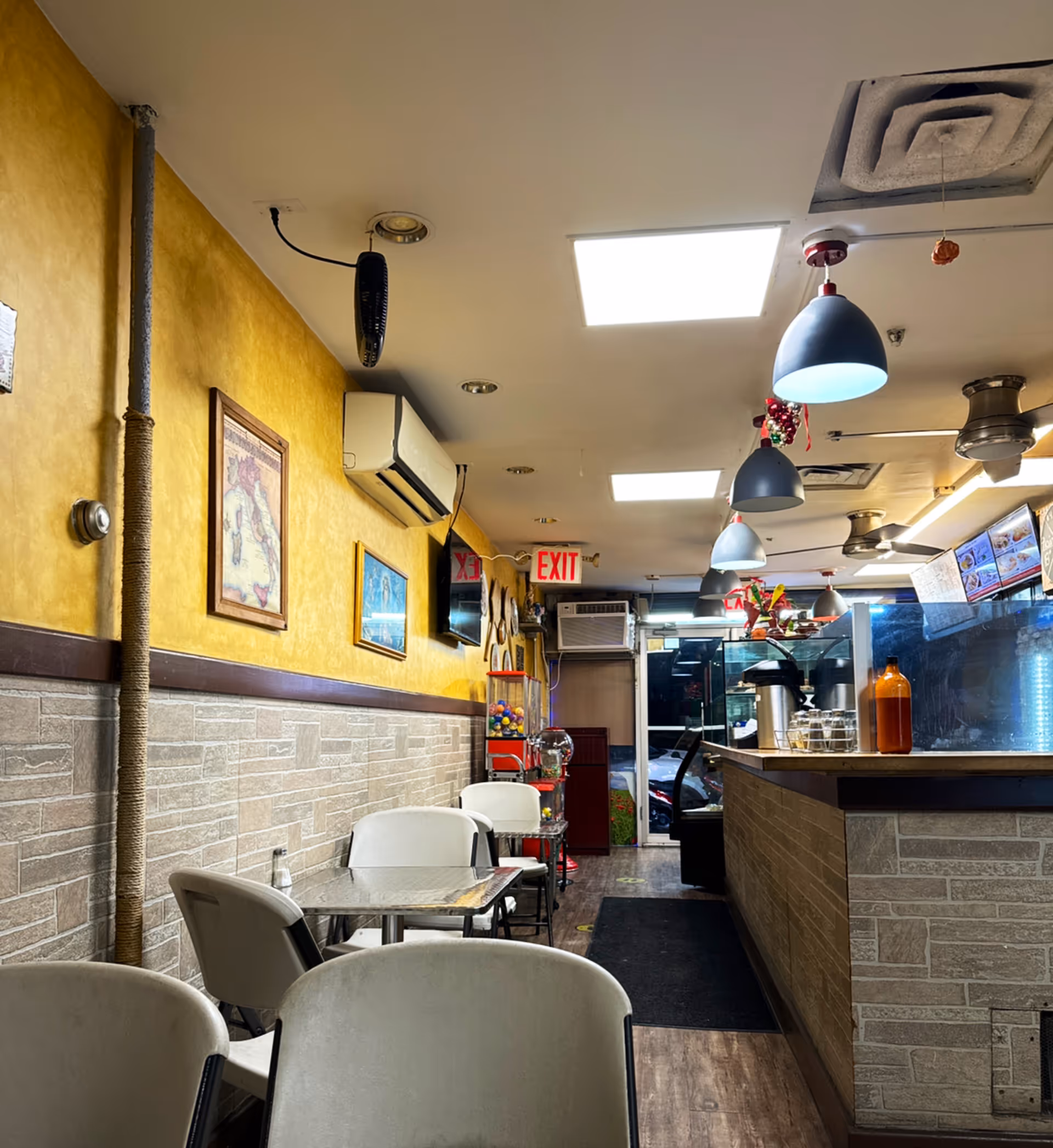Narrow interior dining area with yellow walls, tables, chairs, and a service counter.