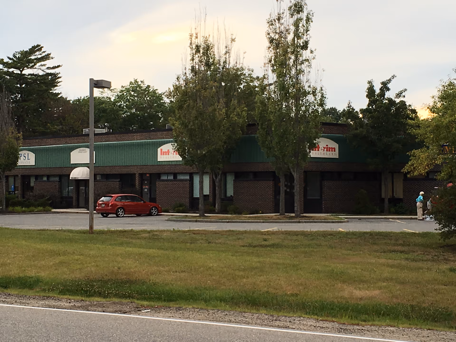 Front view of a single-story brick building with green awning and parked cars.