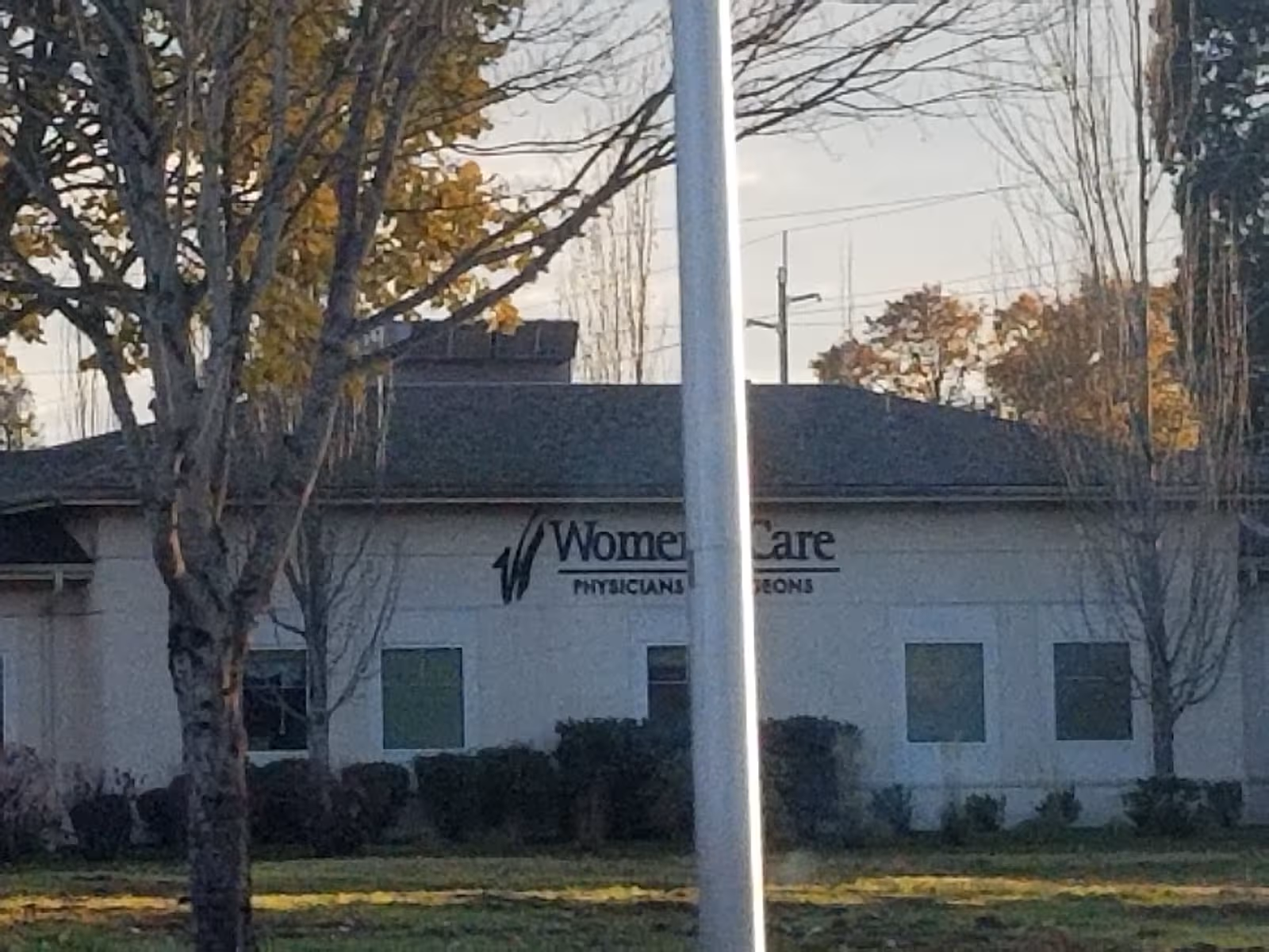 Front exterior of a single-story building with a sign, flagpole, and shrubs.