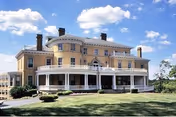 Large two-story manor-style care center with wraparound porch and manicured lawn.