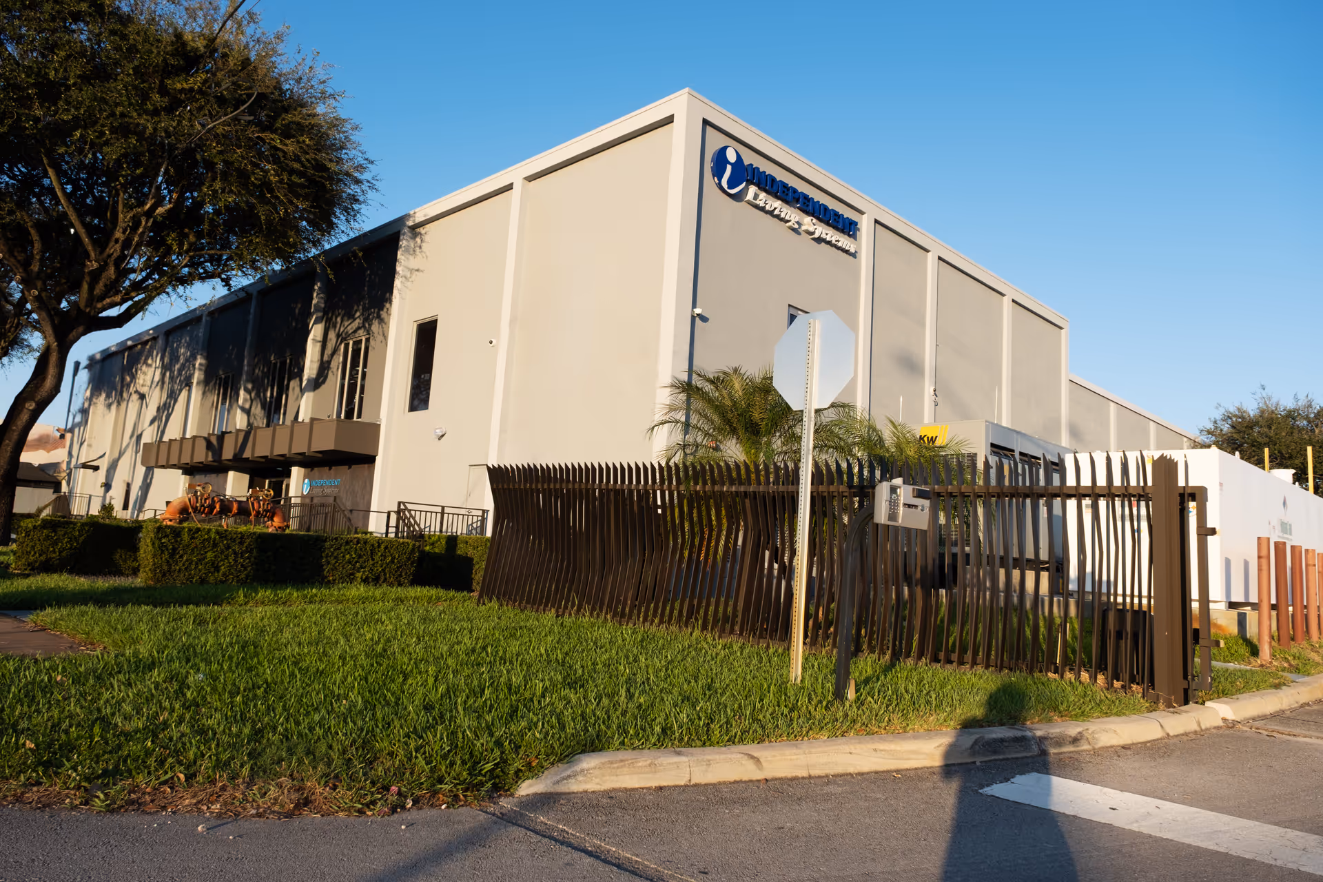A large light-gray senior living facility exterior with a metal fence and palm trees.