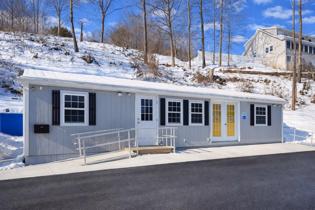 Front view of a small gray building with yellow doors and a ramp in snow