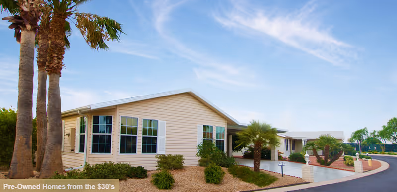 Front view of a single-story beige senior living facility with palm trees and a curved driveway.