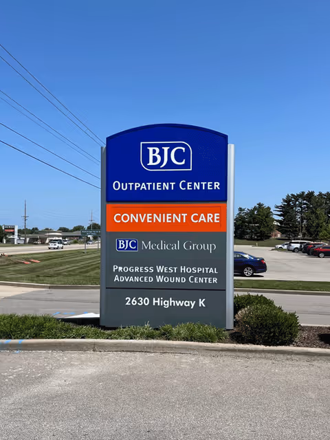 Blue BJC Outpatient Center sign on a grassy area with a parking lot.