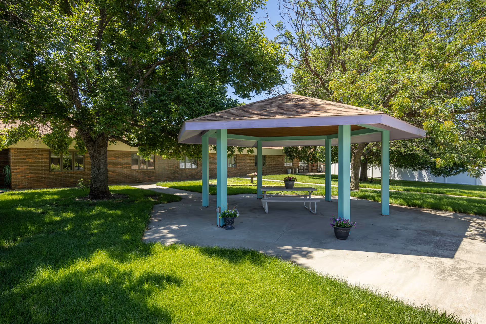 A shaded pavilion with a picnic table in a grassy outdoor area.