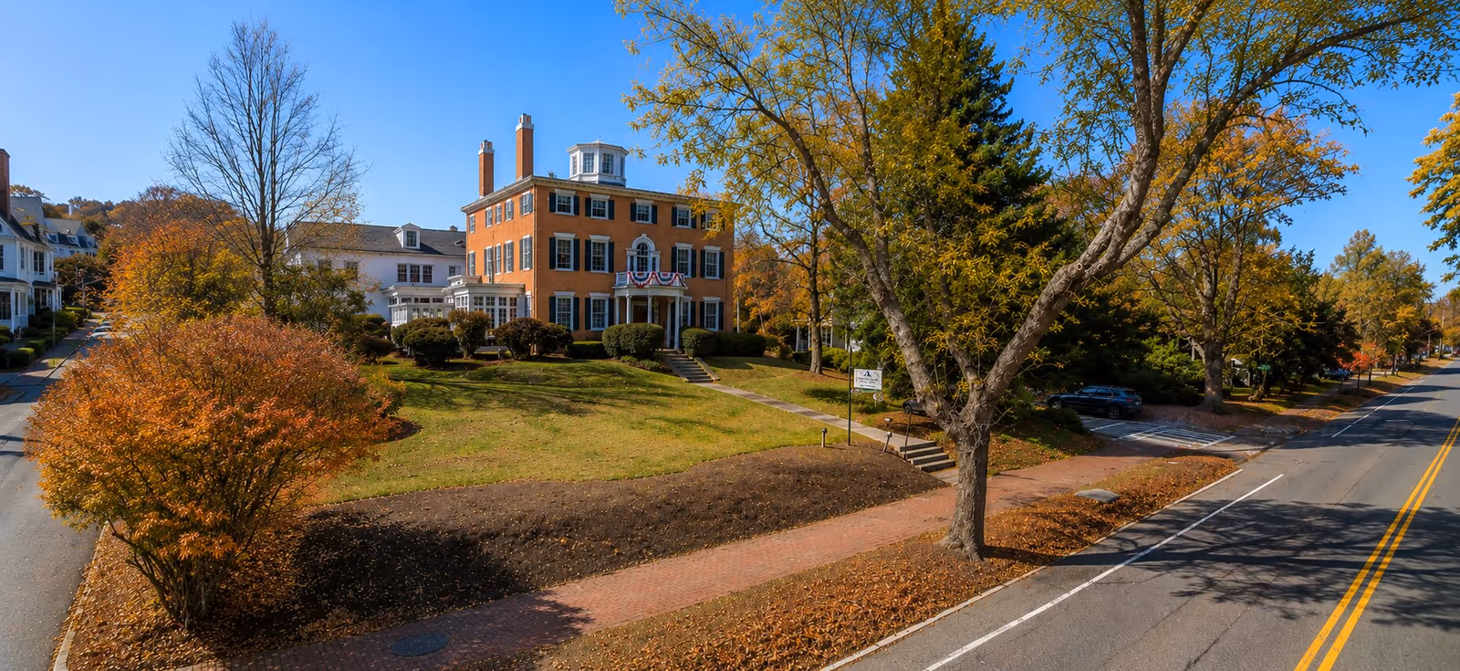 Brick senior living center with autumn trees along a tree lined street.