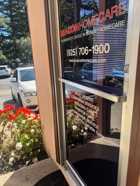Front entrance of Beacon Home Care with glass door, signage, and flowering plants nearby.