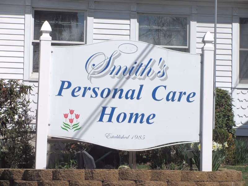 White sign reads Smith's Personal Care Home in front of a gray house.