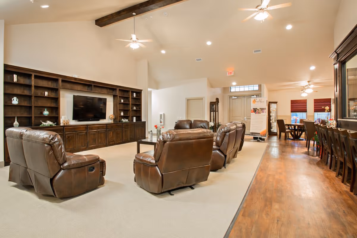 Spacious communal living room with leather recliners arranged facing a wall-mounted TV and built-in shelving, adjacent to a dining area and bar seating.