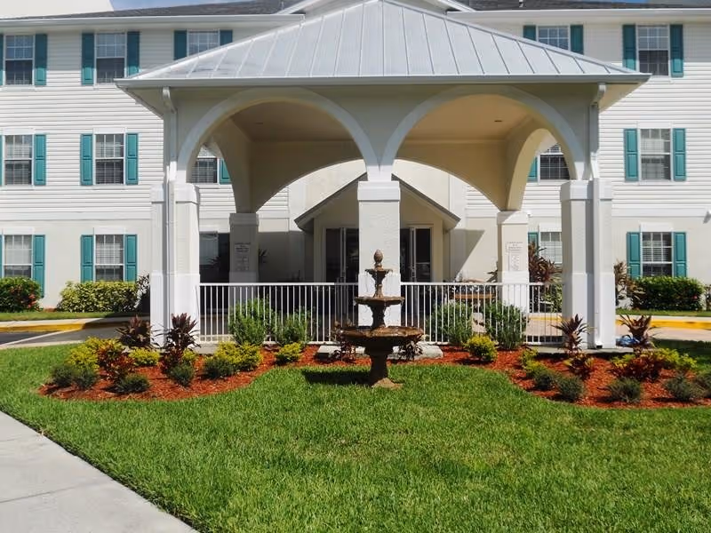 Front view of Fountain Crest Retirement Community with a covered entrance, fountain, and landscaped lawn.