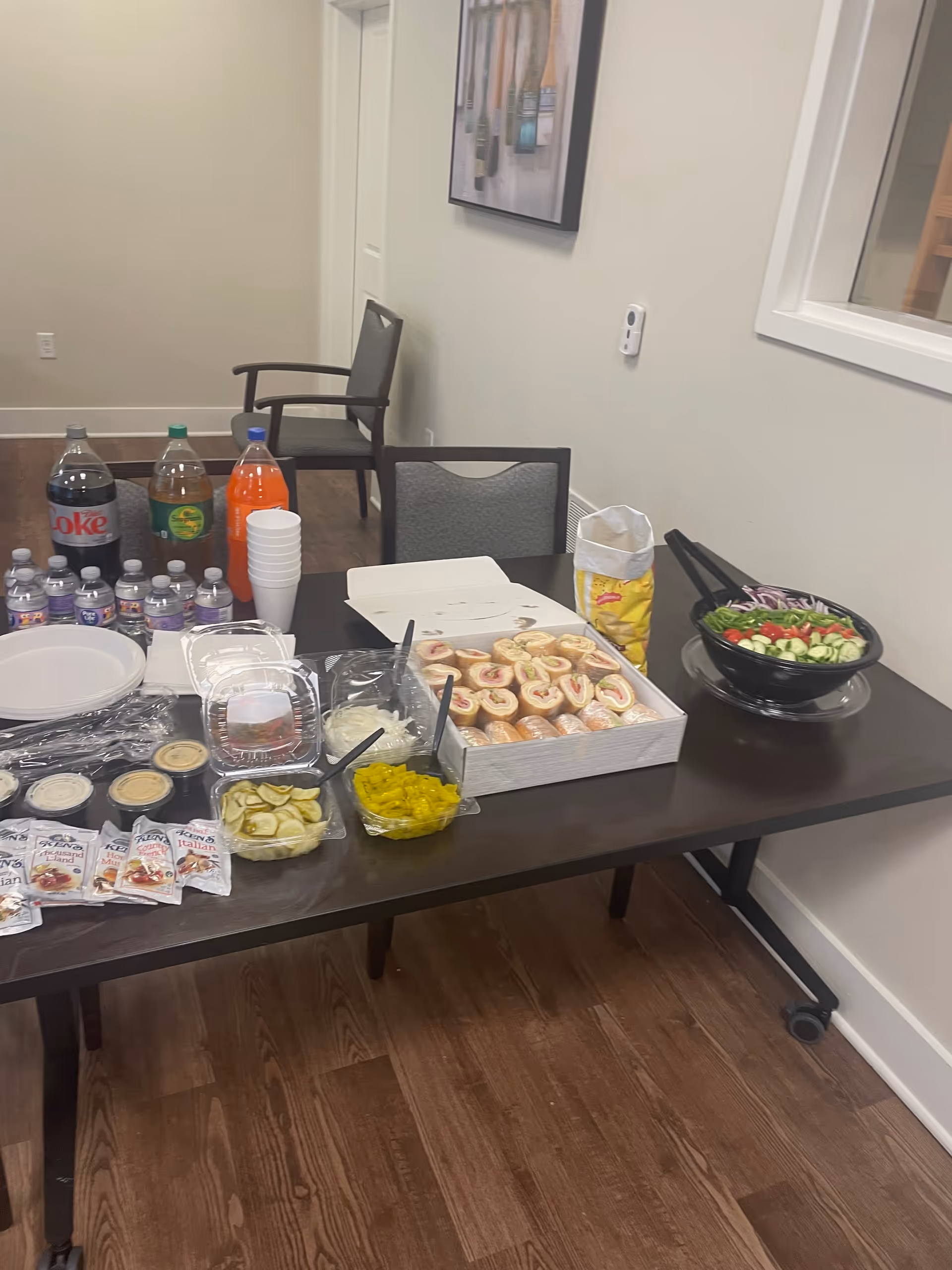 A long table set with snacks, drinks, and plates in a dining area.