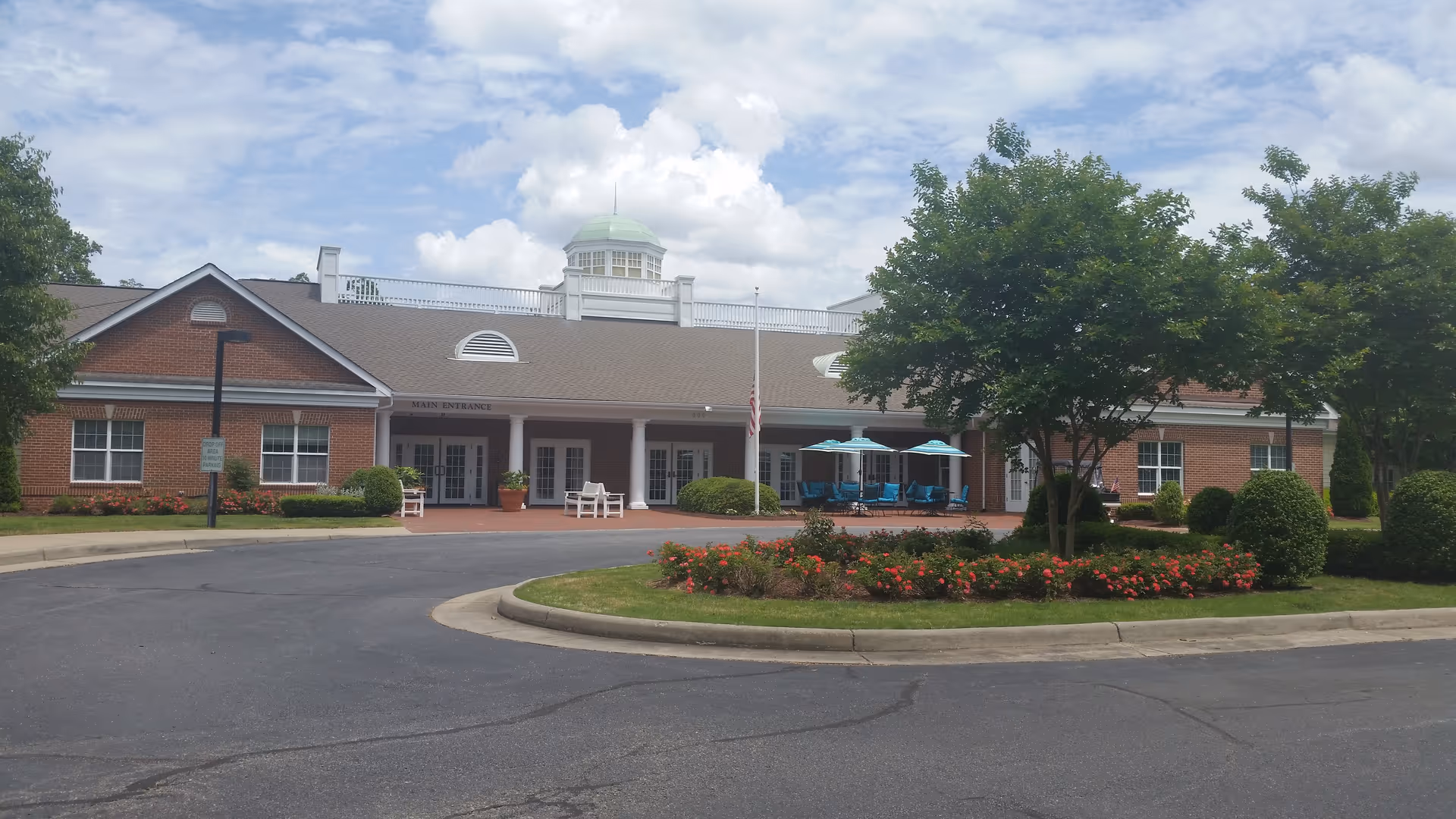 Brick senior living facility with circular drive, main entrance, and landscaped flower beds.