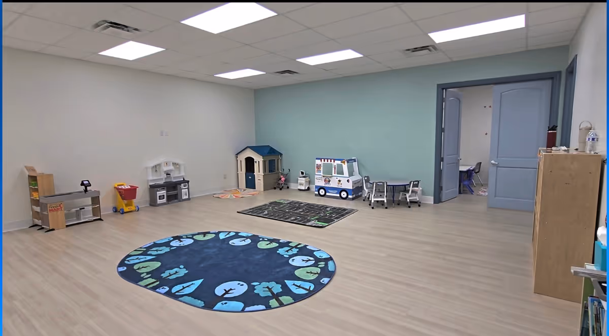 Spacious therapy playroom with toys, a round rug, and child-sized furniture.
