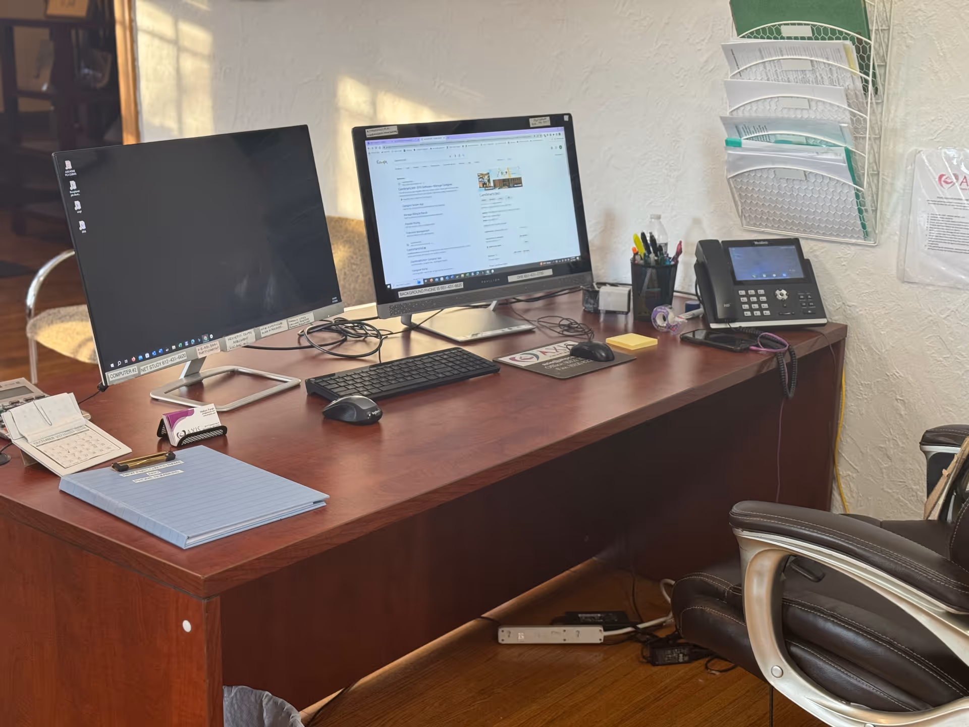 Desk with two computer monitors, keyboard, mouse, and office phone in a facility office.
